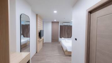 A hotel room with a wooden floor, a large mirror, a TV on a wooden stand, two beds with white linens, and a door with a light switch.