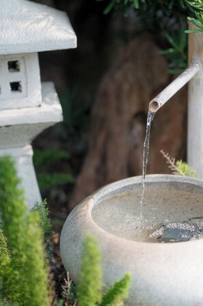 A stone birdbath with water flowing from a spout, surrounded by greenery. - MAYUU AYUTTHAYA HOTEL (Ayutthaya)