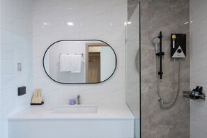 A modern bathroom with a white marble backsplash, a round mirror, a white sink, and a glass-enclosed shower area. - MAYUU AYUTTHAYA HOTEL (Ayutthaya)