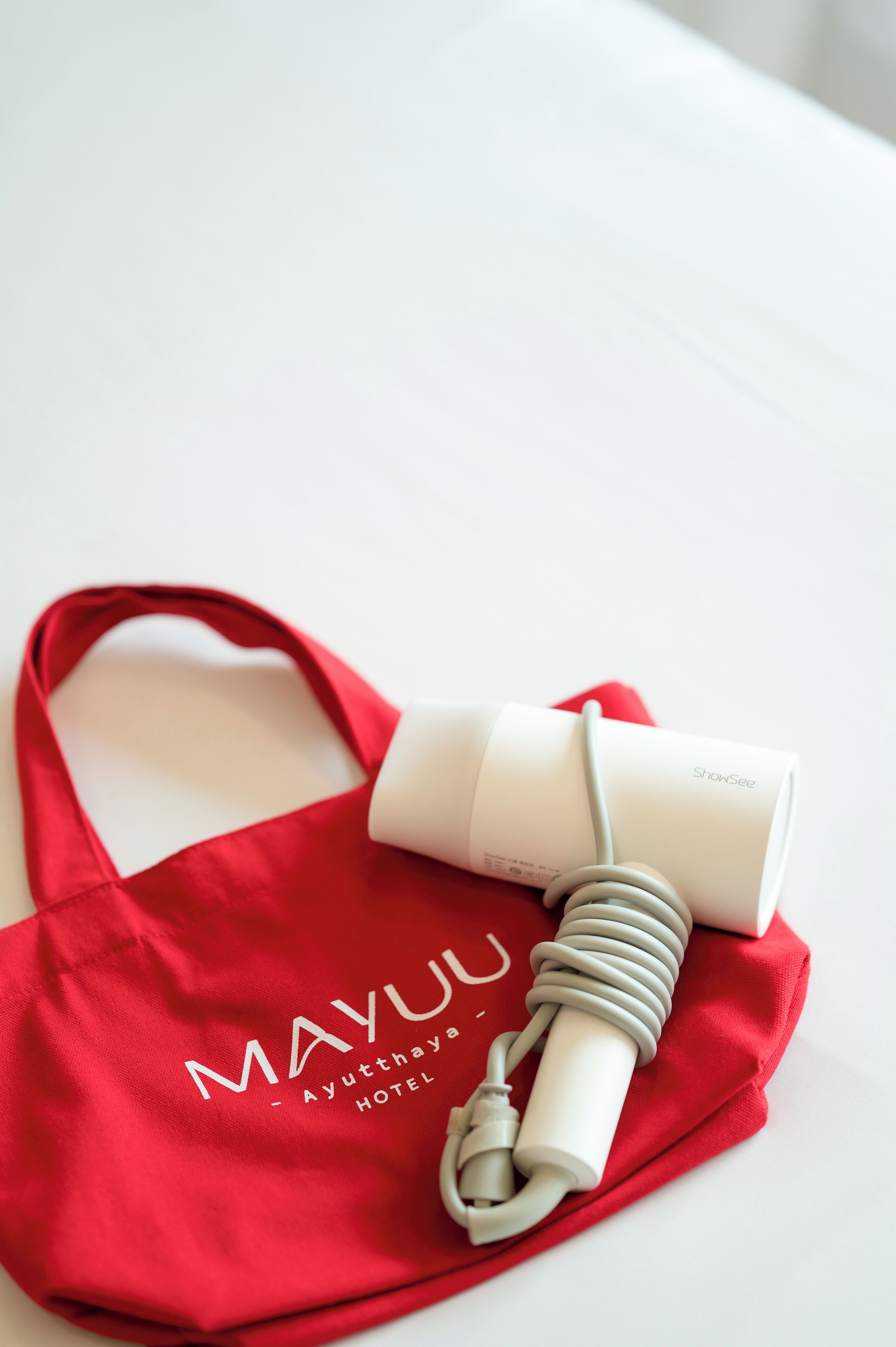 A red bag with "MAYUU - Ayutthaya Hotel" text and a white device with a coiled cable on a white surface.