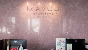 Una recepción en el Hotel Mayu, con un fondo de pared de mármol, un mostrador con computadora, teléfono, buzón de propinas, un dispensador de gel antibacterial y folletos informativos.