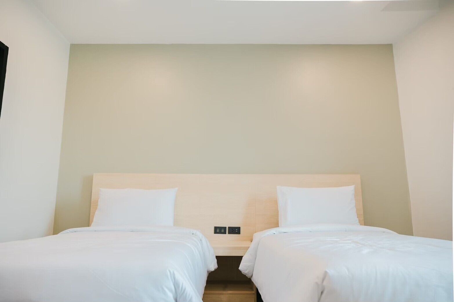 Una habitación de hotel con dos camas individuales, un cabecero de madera y una pared de color neutro.