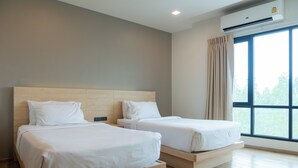 Una habitación de hotel con dos camas individuales, un ventanal con cortinas y un equipo de aire acondicionado.