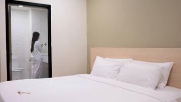 A hotel room with a bed, white linens, a wooden headboard, and a bathroom visible through a glass door.