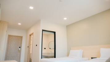 A hotel room with two beds, a wooden door, a bathroom with a mirror, and recessed ceiling lights.