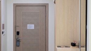 Entrada de una habitación de hotel con una puerta de madera, un escritorio pequeño con un espejo y una lámpara en el techo.