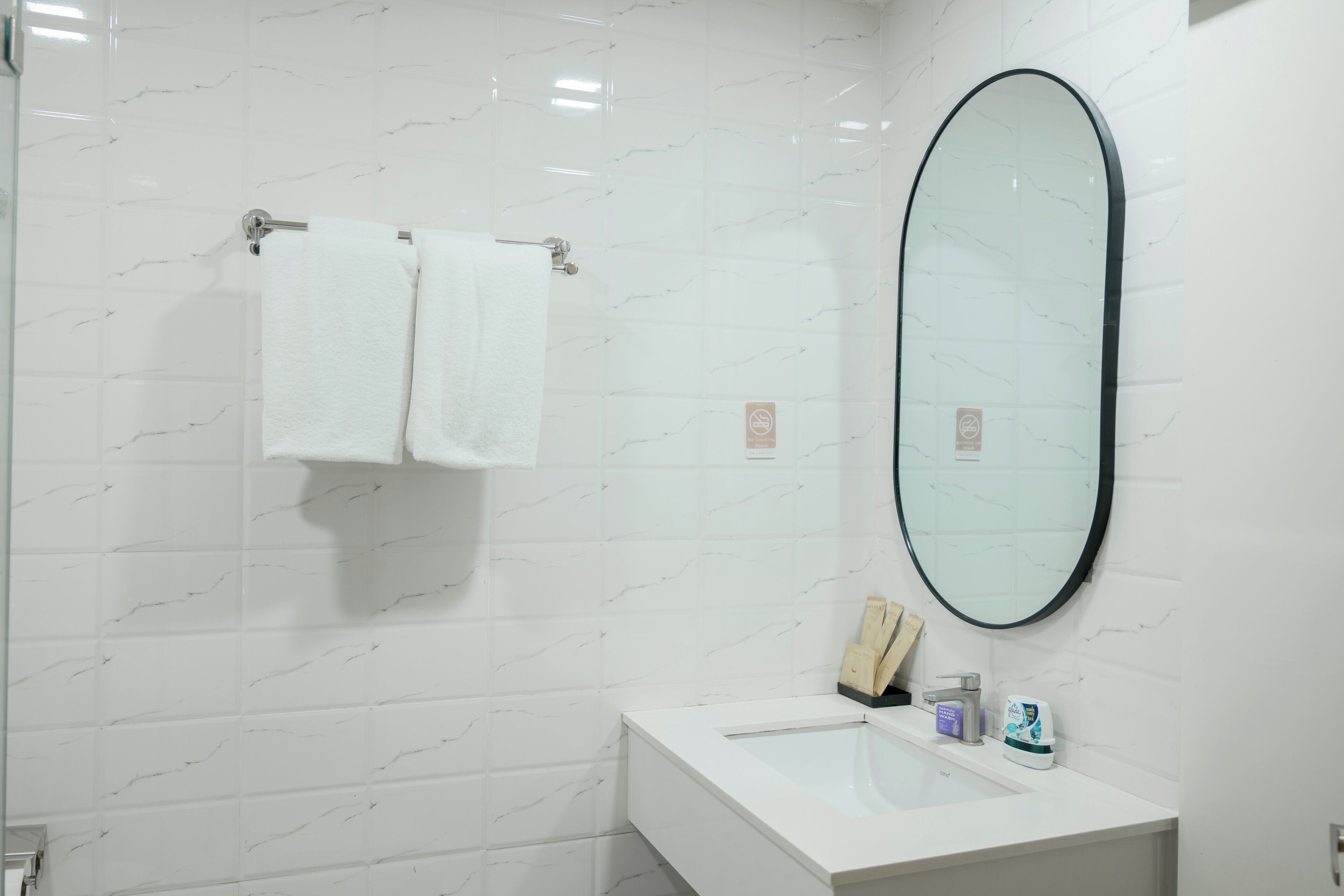 A modern bathroom with white marble tiles, a white sink, a mirror, and two white towels hanging on a towel rack.
