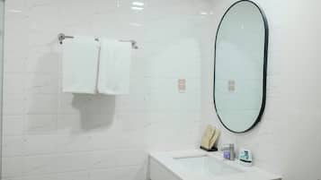 A modern bathroom with white marble tiles, a white sink, a mirror, and two white towels hanging on a towel rack.