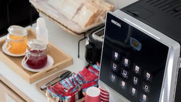 A Nescafe coffee machine with a touchscreen interface, a tray of bread, and a selection of condiments and beverages on a counter.