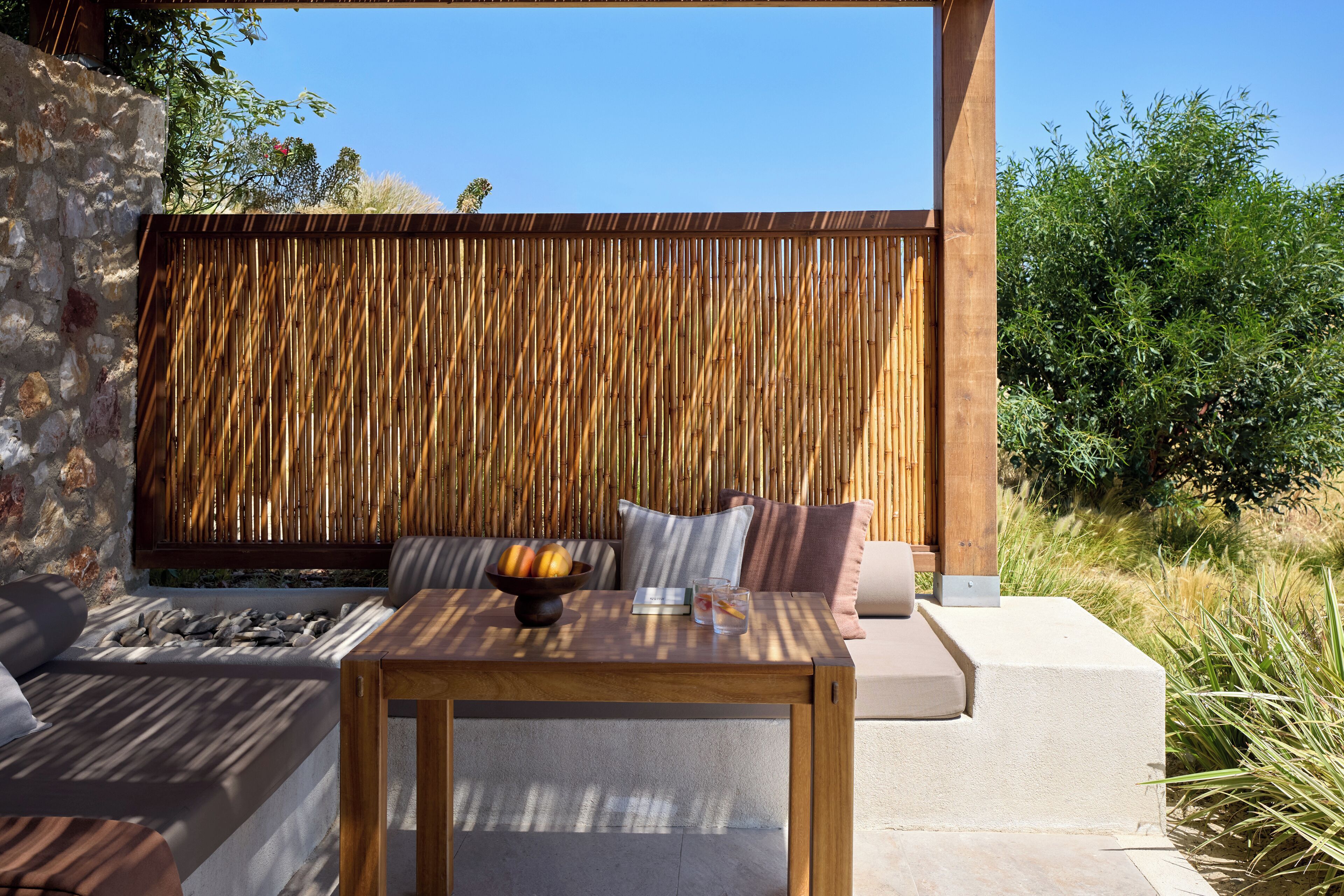 A modern outdoor seating area with a wooden table, cushions, and a stone wall backdrop.