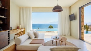 A modern living room with a large sofa, a coffee table, and a view of the sea. - KOIA All - Suite Well Being Resort - Adults Only (Kos)