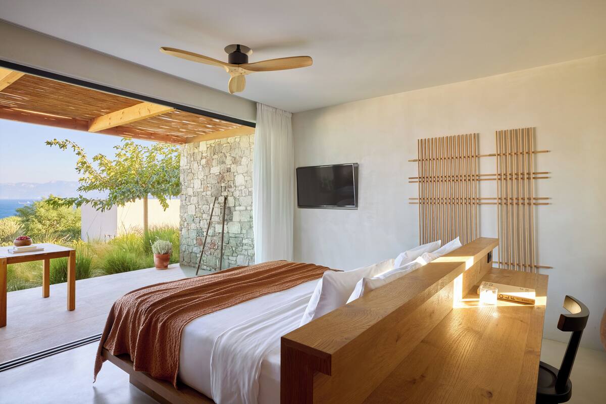 Un dormitorio con una cama, un banco de madera, un televisor y vistas al exterior.