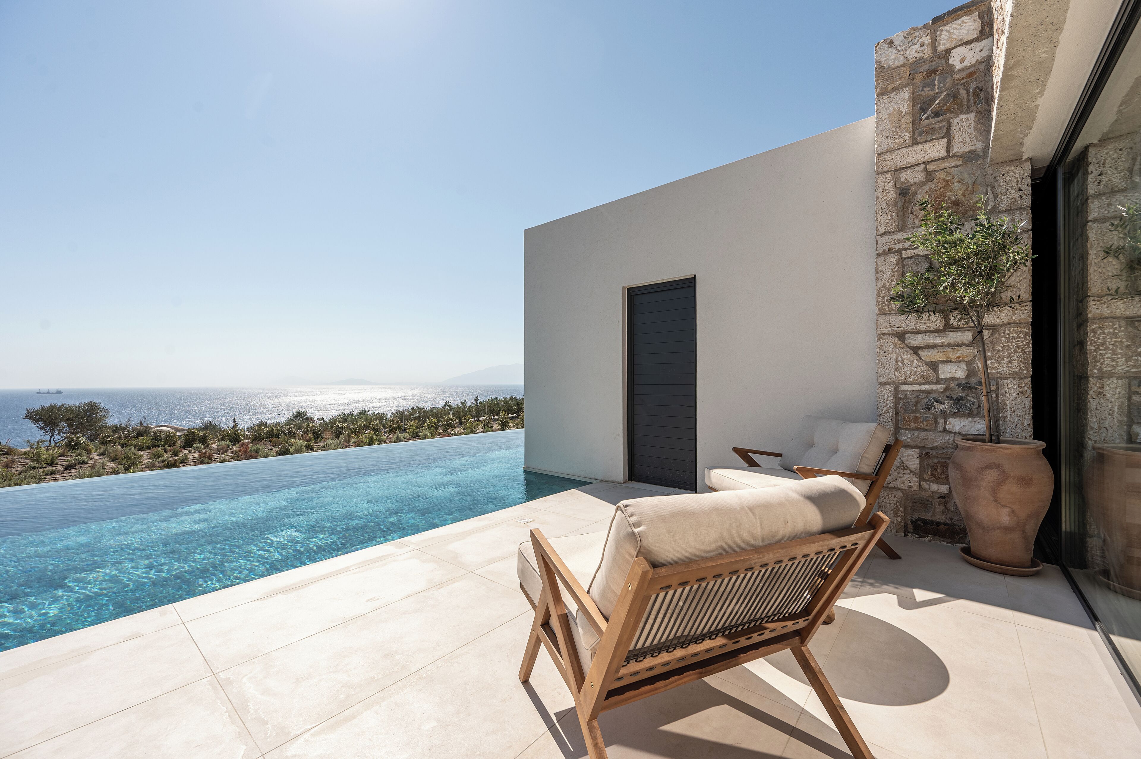 Un espacio moderno de estar al aire libre con piscina, con vistas despejadas al mar y al paisaje distante.