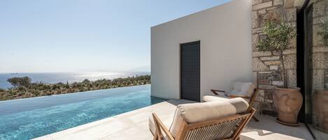 Un espacio moderno de estar al aire libre con piscina, con vistas despejadas al mar y al paisaje distante.