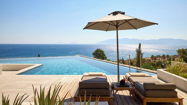A poolside area with lounge chairs and an umbrella, overlooking a clear blue sea and distant mountains. - KOIA All - Suite Well Being Resort - Adults Only (Kos)