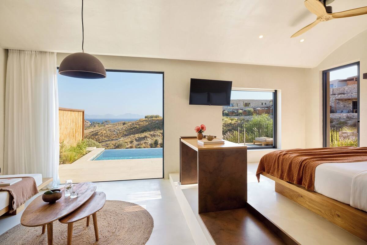 Un dormitorio moderno con una cama grande, un escritorio y vistas a una piscina y al paisaje.