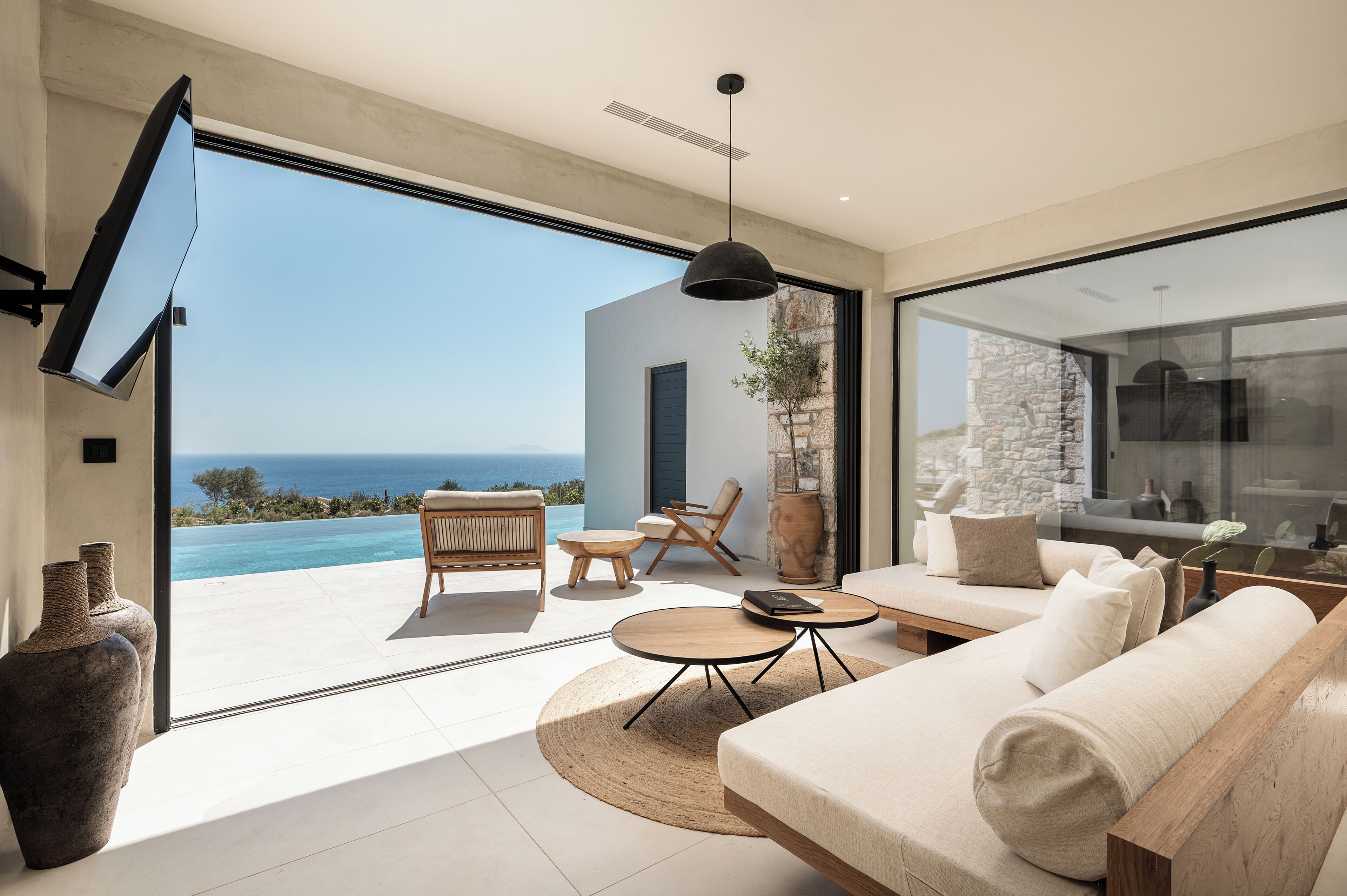 Una sala de estar moderna con un amplio ventanal que da a una piscina, un sofá, una mesa de centro y una zona de comedor.