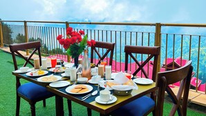 An outdoor dining setup with a table set for breakfast, surrounded by chairs, and overlooking a scenic view. - Fortune Park Kufri, Shimla - Member ITC Hotels' Group (Theog)