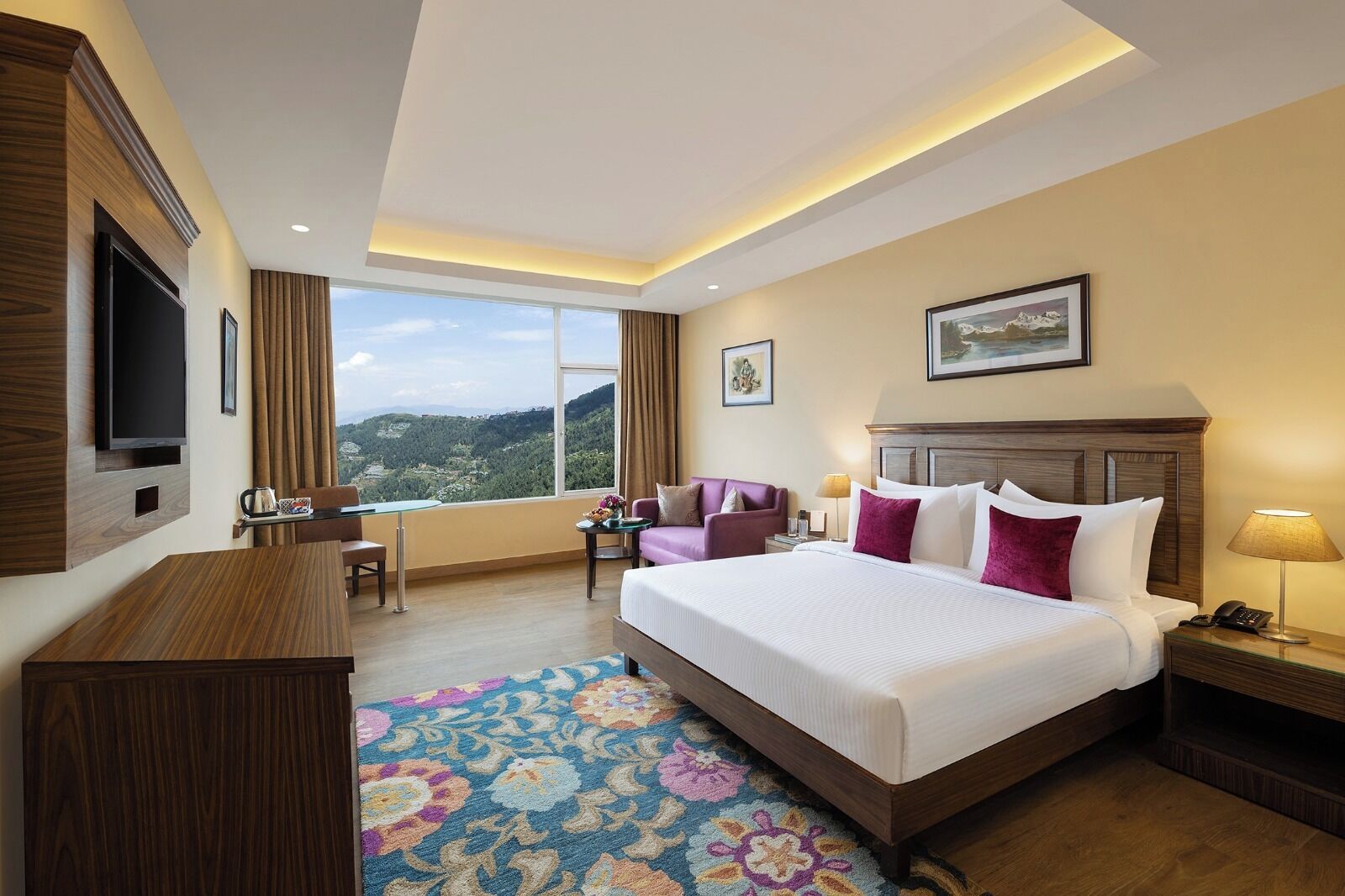 Quarto de hotel com uma cama grande, televisão, escrivaninha, cadeira e vista para as montanhas.