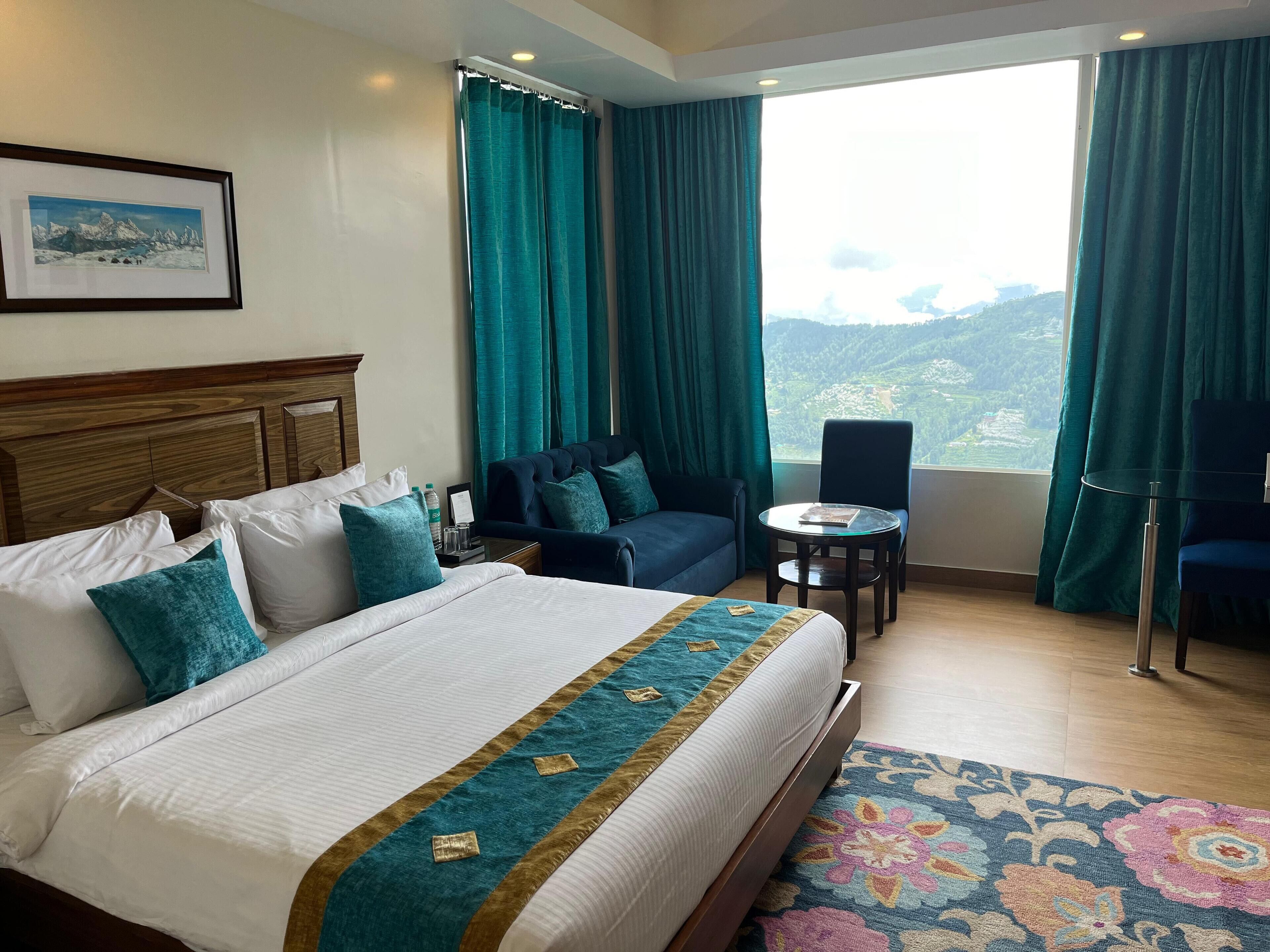 A hotel room with a large bed, a sofa, a small table, and a view of the mountains.