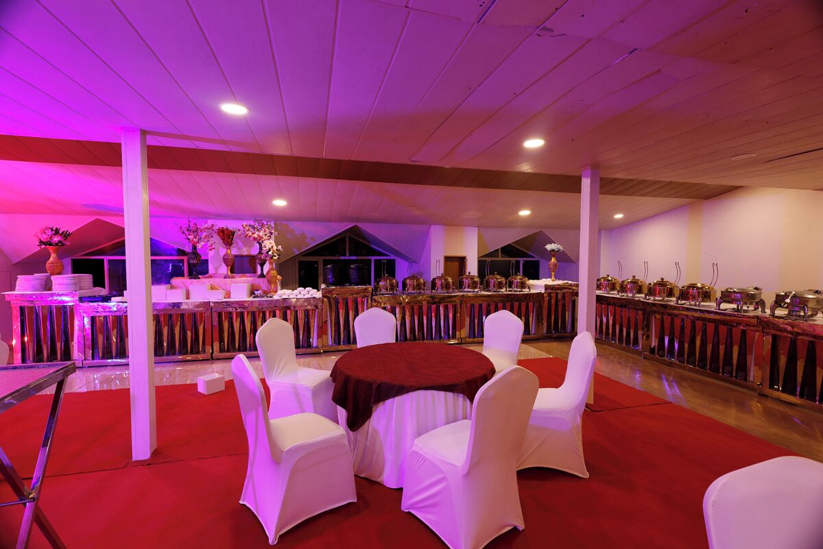 A banquet hall with round tables, white chairs, and a buffet area.