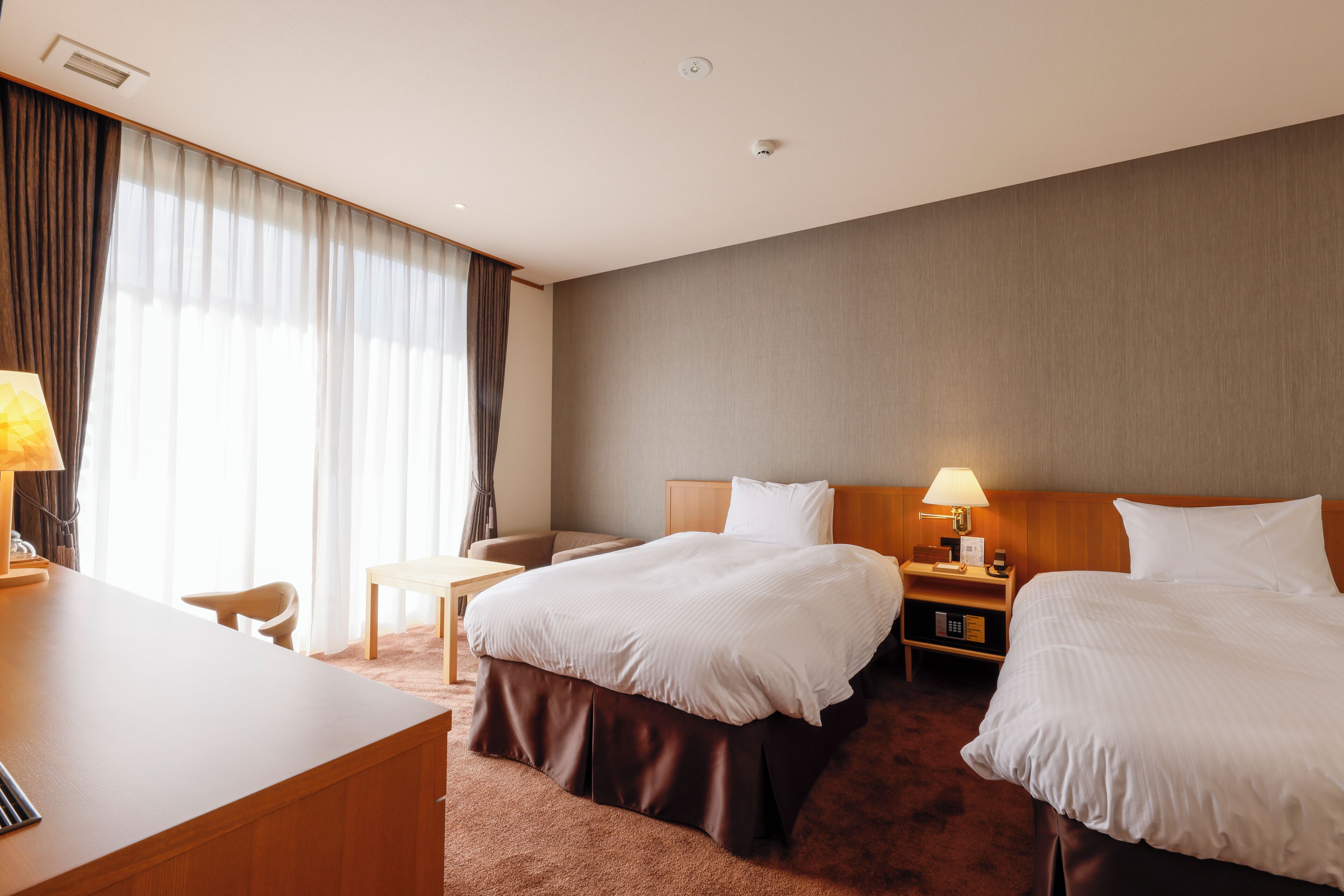 Hotellihuone, jossa on kaksi sänkyä, työpöytä ja tuoli.