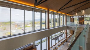 A modern interior with large windows, a staircase, and a seating area with tables and chairs. - Hotel Nara Sakurai No Sato (Sakurai)