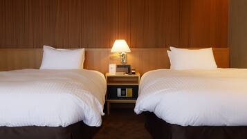 Et hotelværelse med to senge, et sengebord med en lampe og et pengeskab.
