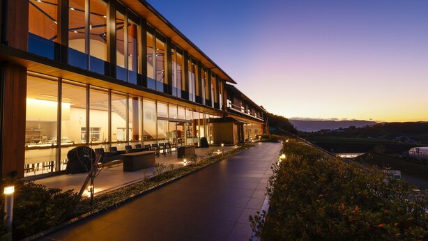 A modern hotel with large glass windows, outdoor seating, and a view of the landscape. - Hotel Nara Sakurai No Sato (Sakurai)
