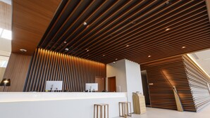 A modern reception area with a wooden slatted ceiling, a white reception desk, and two wooden stools. - Hotel Nara Sakurai No Sato (Sakurai)