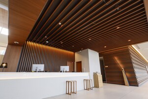 Una moderna zona de recepción con techo de listones de madera, un mostrador blanco y dos taburetes de madera.