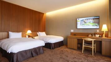 Une chambre d’hôtel avec deux lits, un bureau, une chaise et un téléviseur fixé au mur.