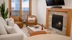 Ein Wohnzimmer mit Kamin, Ledersesseln, einer Couch, einem Couchtisch und einem an der Wand montierten Fernseher.