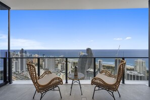 Enjoy a panoramic view of the coastal city from this balcony with two comfortable chairs and a small table.
