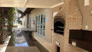 An outdoor patio with a brick fireplace, a covered walkway, and a building with glass doors in the background.
