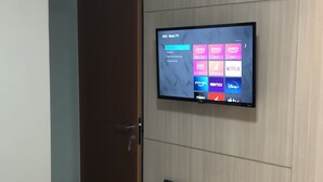 A room with a mounted flat-screen TV displaying streaming services, a wardrobe with a door, and a bed.