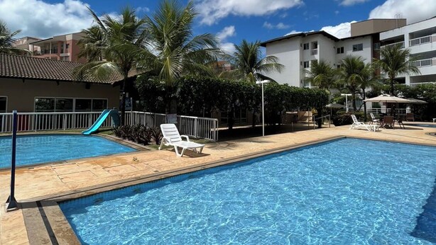 A swimming pool with lounge chairs and a slide, surrounded by palm trees and buildings.