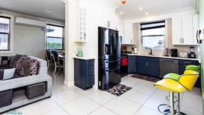 Una cocina moderna con armarios blancos, un refrigerador negro y un comedor con sofá gris y sillas amarillas.