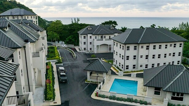 Un barrio residencial con varios edificios de dos pisos, una piscina y una carretera que lleva al mar.
