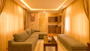 A living room with a sofa, a coffee table, and a kitchen in the background. - Abai Lodges and Spa (Kagio)