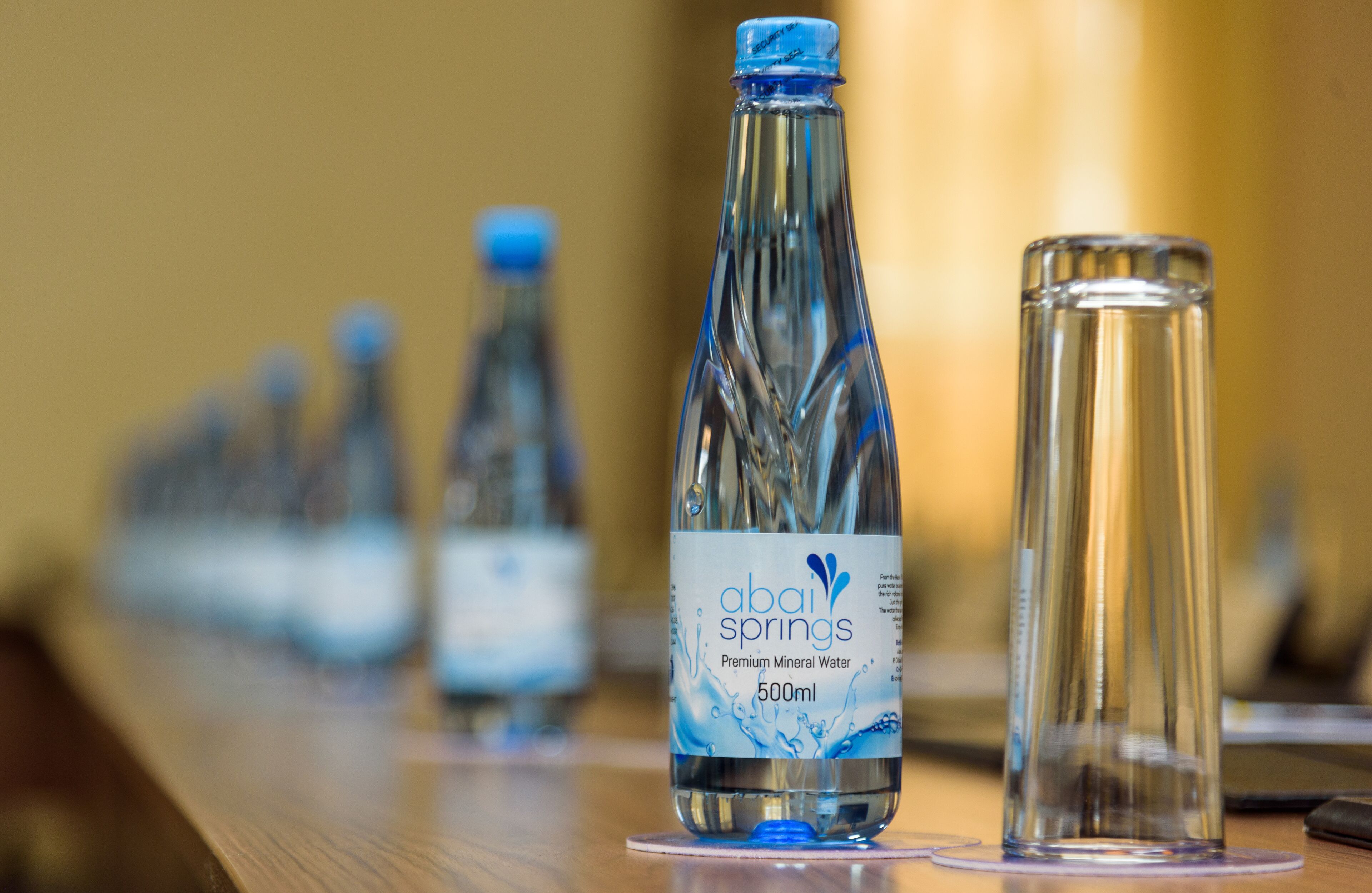A row of clear glass bottles with blue caps labeled "abail springs" and a clear glass tumbler.
