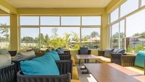 A sunlit outdoor seating area with multiple tables and chairs, large windows offering a view of greenery and buildings. - Abai Lodges and Spa (Kagio)