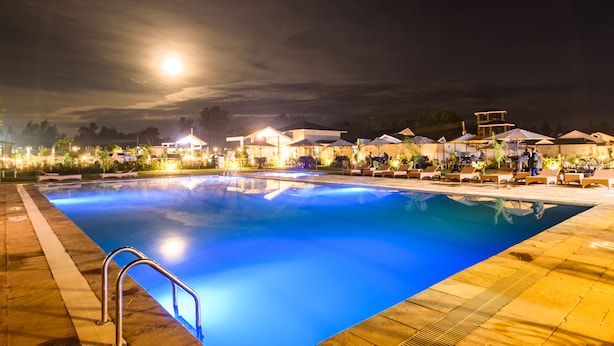 A nighttime swimming pool with a clear view of the pool's edge, a metal handrail, and surrounding lounge areas with umbrellas. - Abai Lodges and Spa (Kagio)