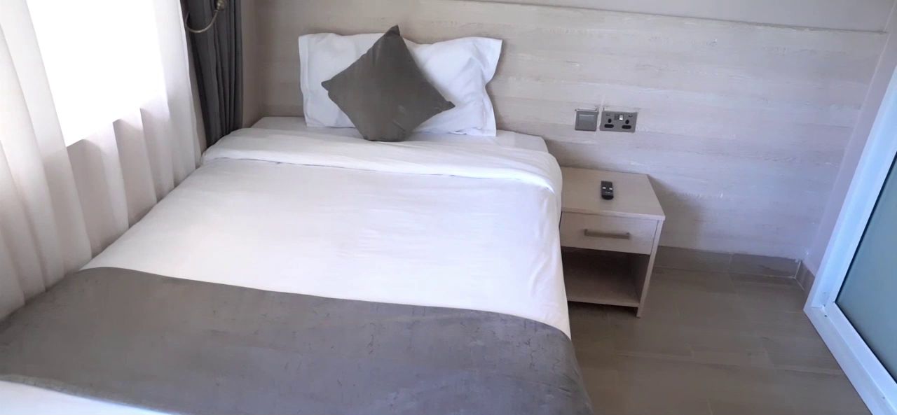 A hotel room with a bed, a nightstand, and a window.