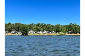 Enjoy lakeside camping with RVs and trailers parked along the shore, surrounded by dense trees.