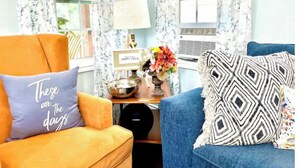 Una habitación con un sofá azul, un sillón naranja y una mesita con una lámpara y un florero.