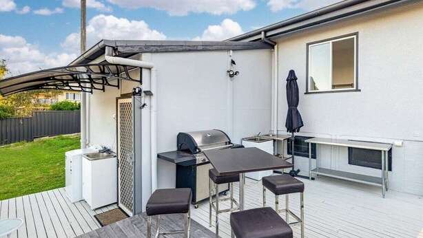 Een terras buiten met een barbecue, barkrukken en een tafel.