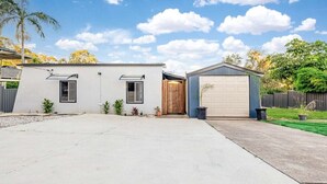 Een huis met twee verdiepingen, een garage, een klein tuinhuisje en een verharde oprit.