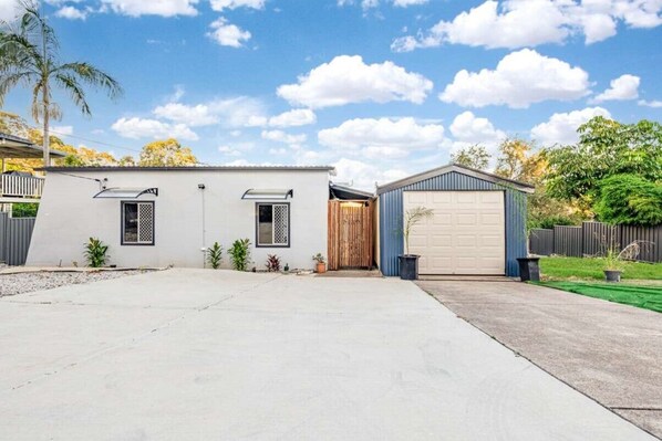 Une maison à deux étages avec un garage, un petit abri attenant et une allée pavée.