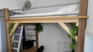 Een kleine kamer met een stapelbed, een bureau, een stoel en een radiator.